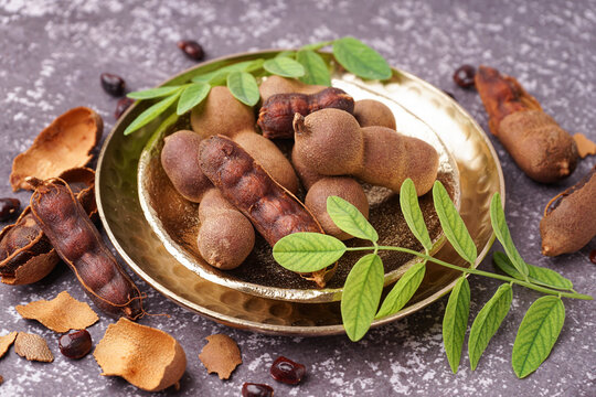 Plates of tasty tamarinds, leaves and seeds on grey background