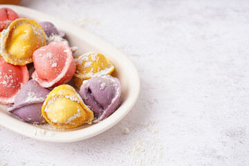 Plate with colorful raw dumplings on white background