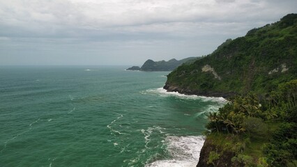 Aerial drone view of coastline with hills and trees, as well as view of coral cliffs and sea with waves from the ocean in Sagara view also known as Karang Bolong Beach Kebumen Central Java Indonesia