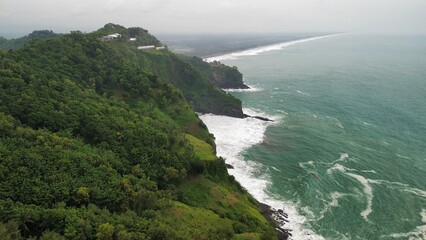 Aerial drone view of hills with trees and fertile agricultural land bordering the ocean and countryside in Indonesia