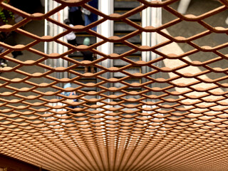 Metal mesh creates a grid - Close-up shot of a metal fence mesh grid with an escalator visible through it