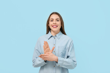 Young deaf mute woman using sign language on blue background