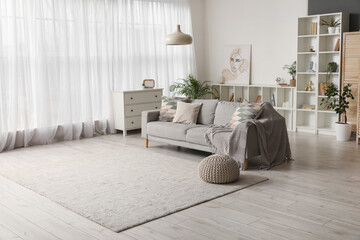 Stylish interior of living room with comfortable sofa, shelving units and chest of drawers