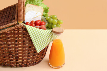 Wicker basket with tasty food and juice for picnic on table against beige background