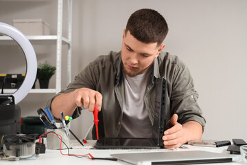 Male technician with screwdriver repairing laptop at table in service center
