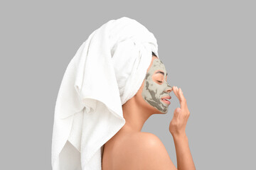 Young African-American woman with clay facial mask on grey background