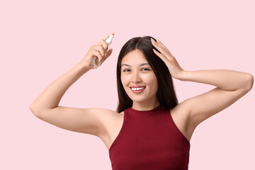 Fototapeta premium Beautiful young happy woman applying hair spray on pink background