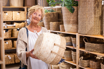 Positive mature woman choosing wicker basket for a country house in hardware store