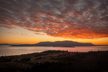 Dramatic and colorful sunset over Orcas Island in the San Juan Islands archipelago of Washington State. Aerial drone view of an amazing cloudscape as seen from Lummi Island located in the Salish Sea.