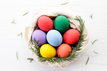Colorful Easter eggs in a basket on white wooden table.