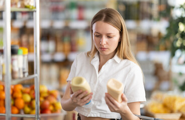 Young woman buyer chooses mayonnaise sauce in grocery store