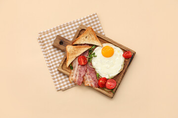 Board with tasty fried egg, tomatoes, toasts and bacon on beige background. Top view
