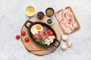Pan with tasty fried egg, bacon, mushrooms, tomatoes and spices in bowls on wooden stand on white grunge background. Top view