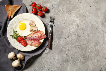 Plate with fried egg, bacon, mushrooms and tomatoes on grey background. Top view