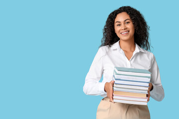 Beautiful young African-American woman with stack of books on blue background