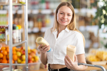 Young woman buyer chooses mayonnaise sauce in grocery store