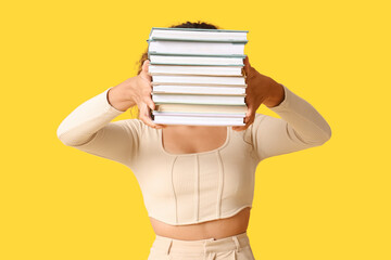 Young woman with stack of books on yellow background
