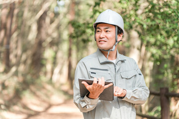 公園・森林で樹木をチェックする作業着姿の林業の男性
