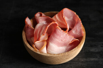 Tasty bacon slices in bowl on black background