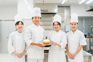 厨房・キッチンに立つコックコート姿の調理師・シェフ・コックの男女
