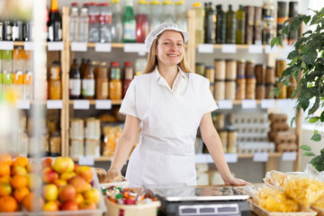 Young female seller in apron standing at counter in grocery store