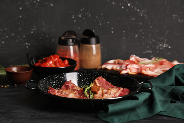 Tasty fried bacon in frying pan on table against black background