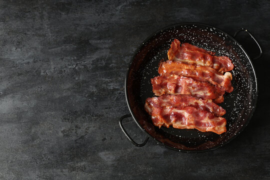Frying pan with fried bacon rashers on black background