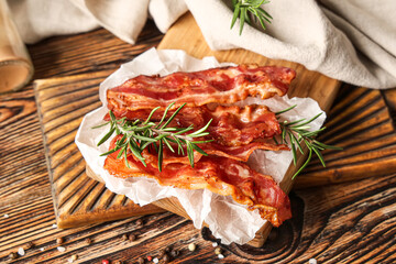 Cutting board with fried bacon rashers and rosemary on wooden background