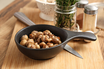 Frying pan with roasted mushrooms on wooden table
