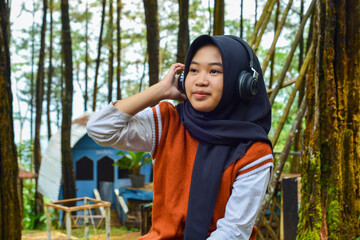 Naklejka premium Beautiful woman asian muslim standing in front of a fresh forest park with smart phone and headphones