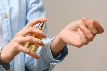 Young woman applying perfume on grey background, closeup