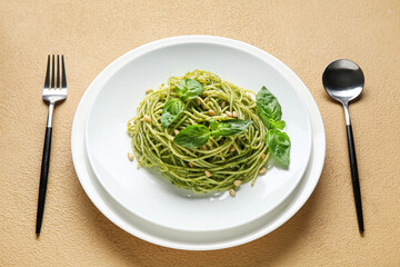 Plate of tasty pesto pasta with pine nuts, basil leaves and cutlery on beige background