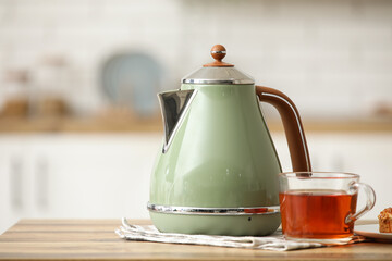 Modern electric kettle and glass cup of hot tea on wooden table in kitchen