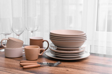 Clean dishes and cutlery on wooden table near window in kitchen