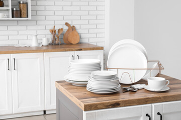 Holder with clean white plates and cutlery on counter in kitchen