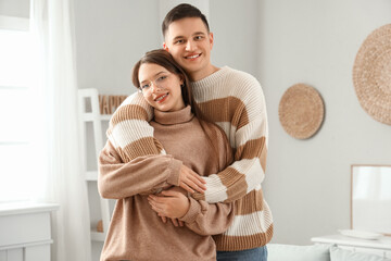 Cute young couple in warm sweaters hugging at home