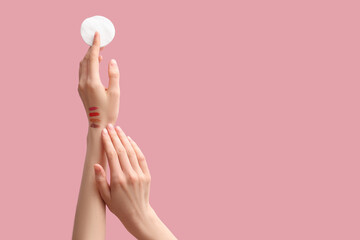 Female hands with cosmetic samples holding cotton pad on pink background