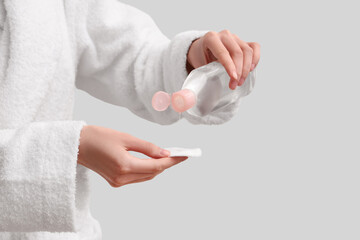 Young woman with cotton pad and bottle of micellar water near white wall