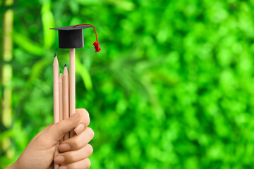 Woman holding pencils with graduation hat outdoors, closeup. Student loan concept