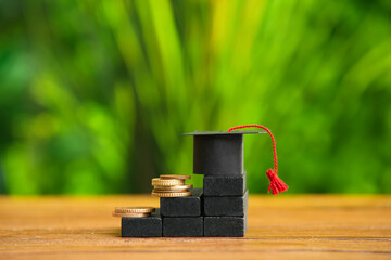 Blocks with coins and graduation hat on table outdoors. Student loan concept