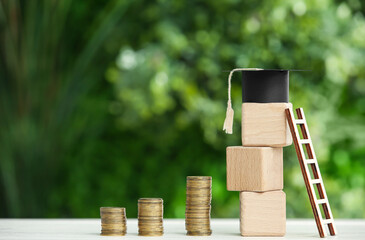 Cubes with graduation hat, ladder and coins on table outdoors. Student loan concept