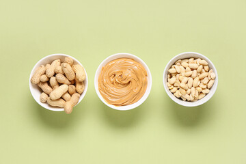 Bowls with nuts and tasty peanut butter on green background