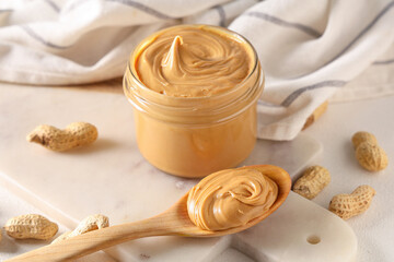 Jar and wooden spoon of tasty peanut butter with nuts, closeup