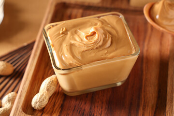 Wooden boards with bowl of tasty peanut butter and nuts, closeup