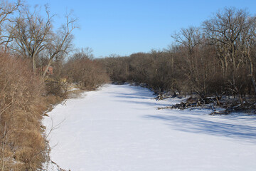Snow covered frozen Des Plaines River on a sunny day at Camp Ground Road Woods in Des Plaines, Illinois