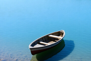 Obraz premium A small wooden rowboat drifts peacefully in a calm, crystal-clear lake