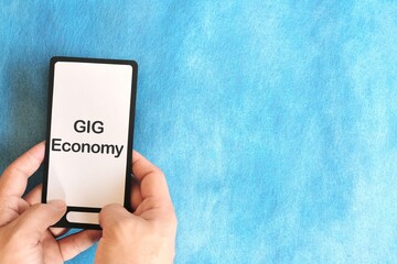 Human hand holding mobile phone with written phrase gig economy. Gig economy concept.