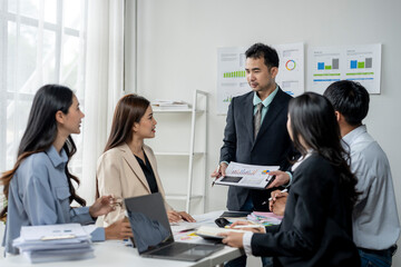 A group of people are gathered around a table with papers and laptops