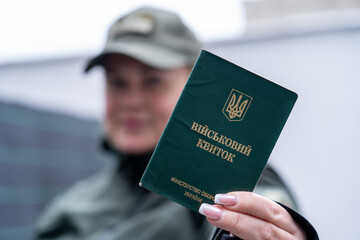 A girl in a military uniform with a manicure holds a military registration document (military ID,...