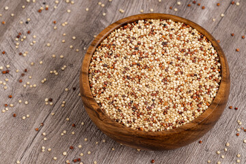Wooden bowl filled with mixed quinoa grains, featuring white, red, and black seeds, placed on a rustic wooden surface. Ideal for healthy food and nutrition projects.